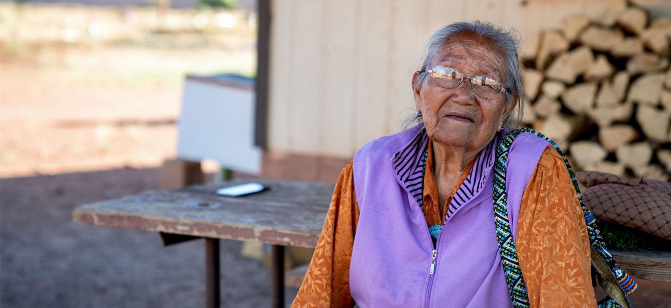 A senior Navajo, American Indian woman is looking at the camera solemnly. 