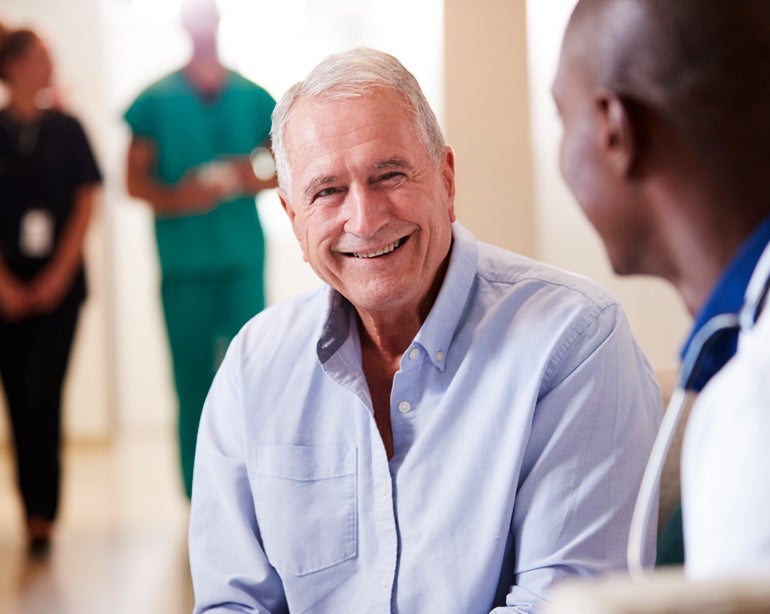 A senior Caucasian man is talking to a healthcare professional, smiling.