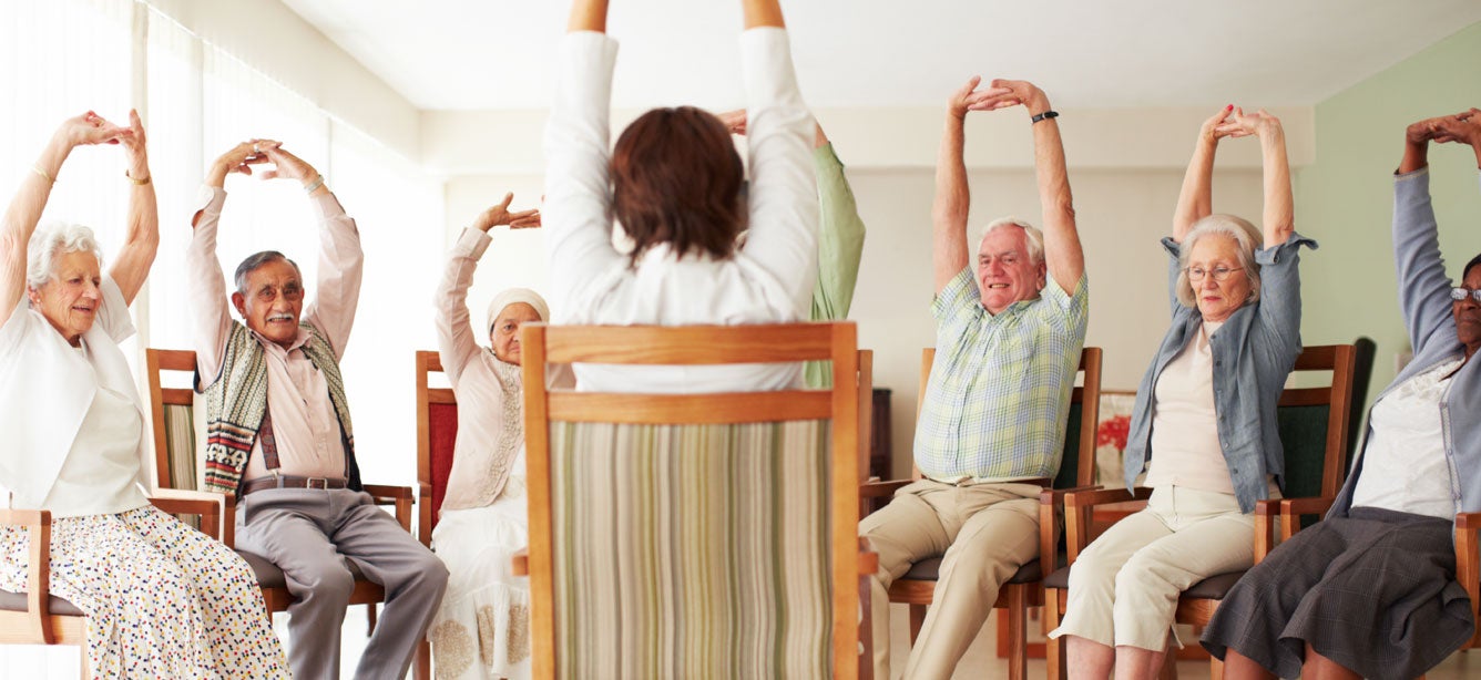 A group of older adults are going through their daily stretching exercise routine at a senior center.