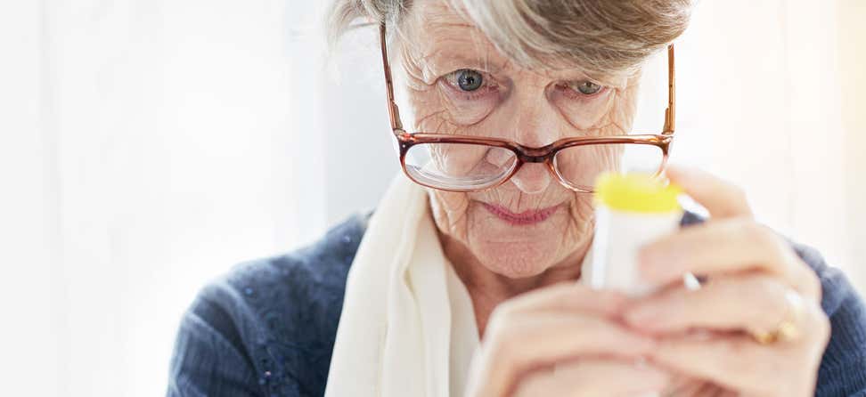 Senior woman peers through her glasses, trying to read instructions on a prescription bottle.