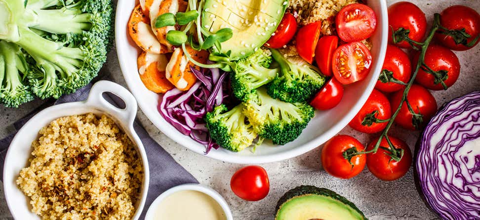 A Buddha bowl salad surrounded by healthy, fresh ingredients on a table.