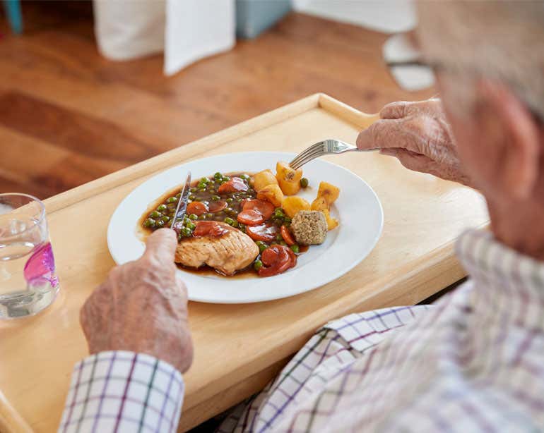A senior Caucasian man is eating a well-balanced dinner at his table.