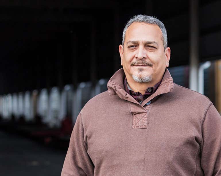 An older Hispanic working male is outside at a shipping port.