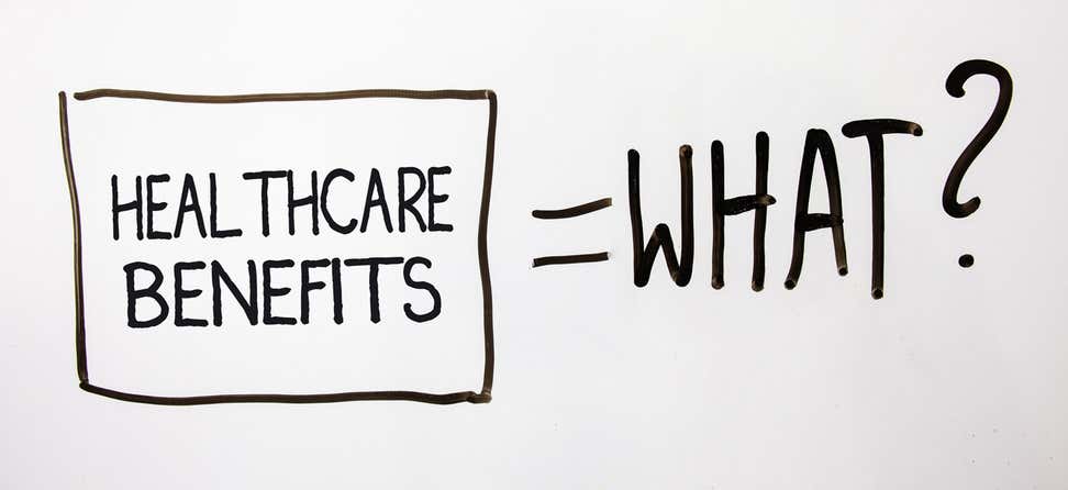 A close up shot of a whiteboard that has "healthcare benefits" inside a box with an equal sign and the word "what?" next to it, indicating confusion over what healthcare benefits are.