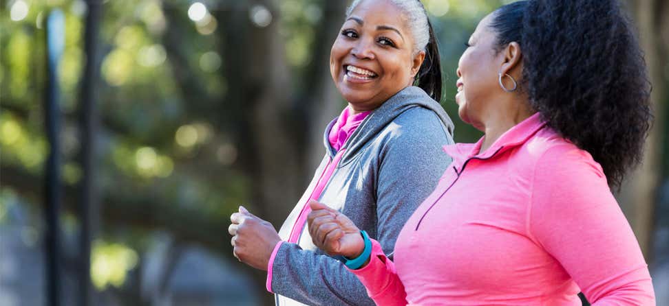Two Black senior women are out exercising while smiling and talking to each other.