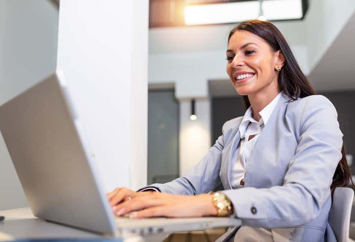 A Hispanic woman professional sits at her laptop while speaking to others during a conference.