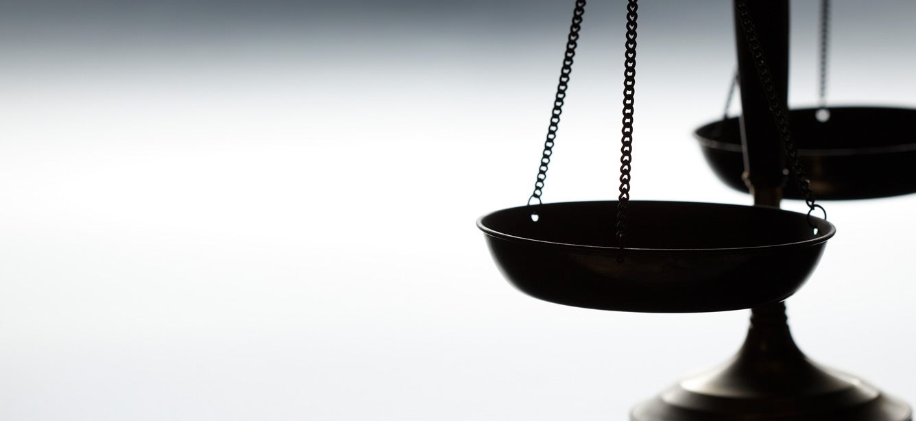 A scale of justice sits alone over the right of the frame unbalanced.
