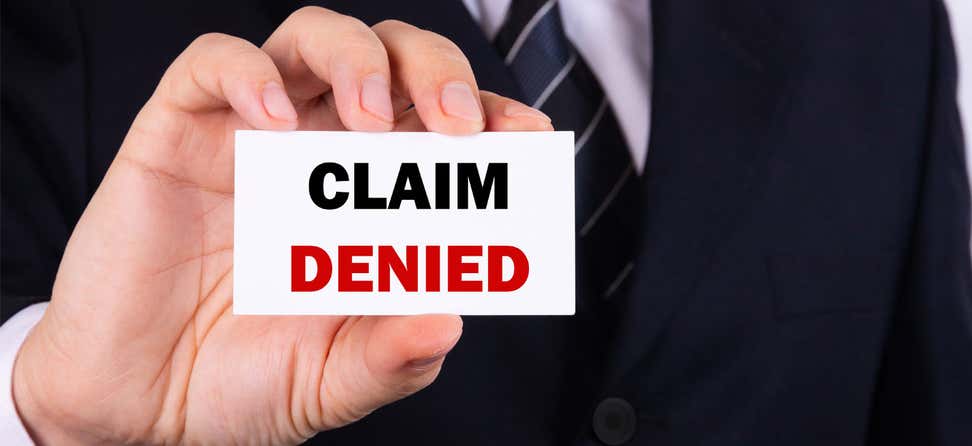 A man is holding a card in his hand that said "Claim Denied".