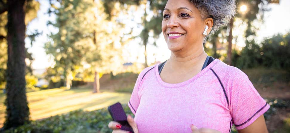 A Black senior woman is smiling while going for a run in the park.