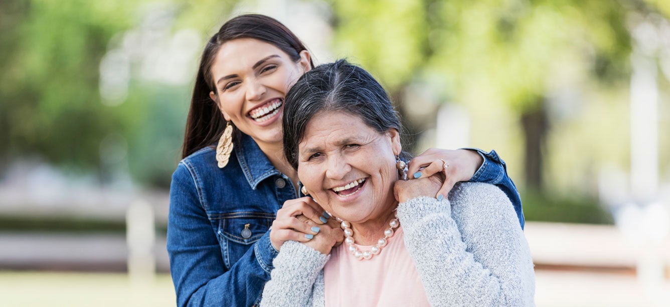 Hispanic daughter puts hands on shoulder of her older mother, both smiling