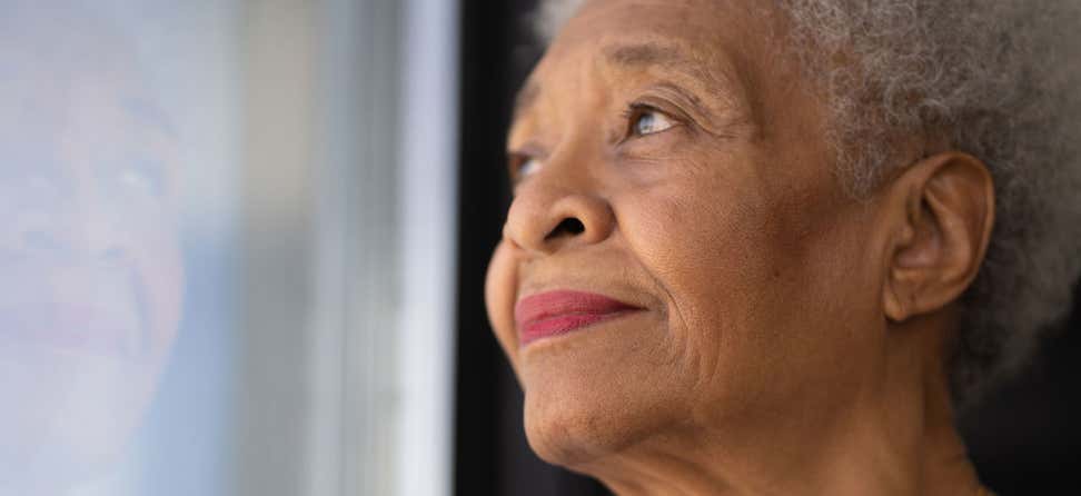 A lonely Black senior woman is looking out of her window.
