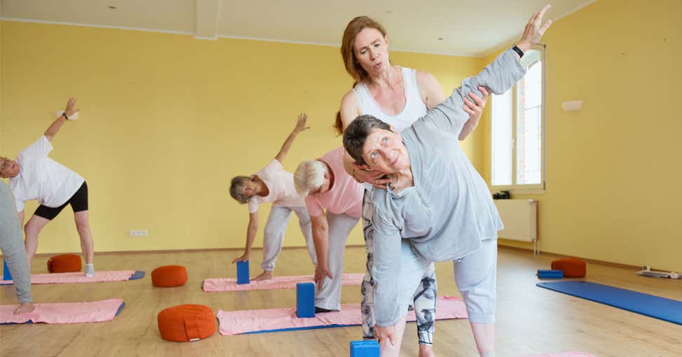 A senior Caucasian woman is getting help from her instructor during her yoga class at a local senior center.