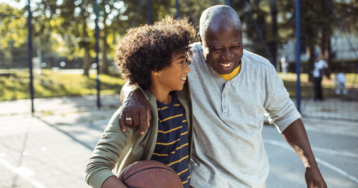 A senior Black man is outside playing basketball with his grandson.