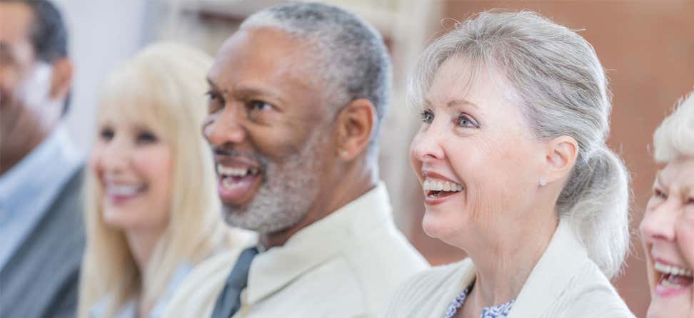 A diverse group of senior center professionals are at a continuing education conference, where one senior woman is raising her hand.