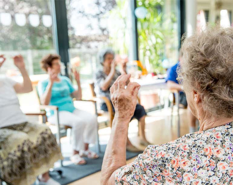 A senior woman and other older adults are playing a group activity, exercising together in a senior center.