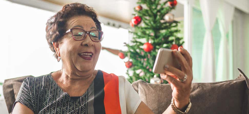 A senior Asian woman is holding her phone video chatting with a loved one during the holiday.