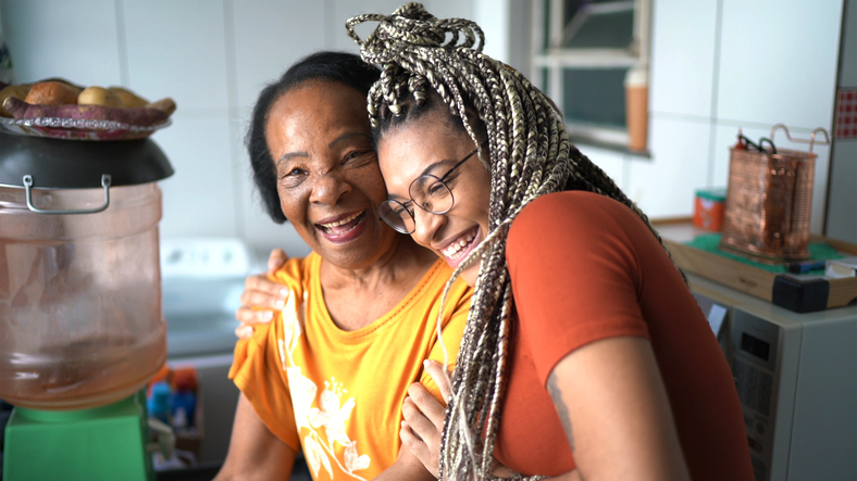 A young African American woman with braids hugs an older African American woman while both laugh