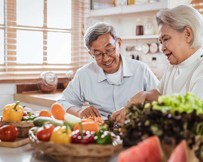 A senior Asian couple is cooking a healthy meal together in their kitchen.