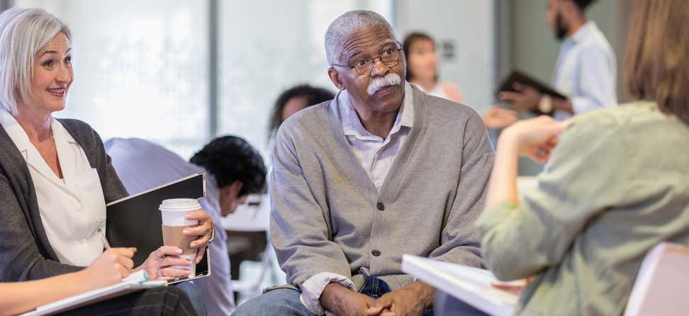 A Black senior man is sitting in a group having a discussion with other older adults.