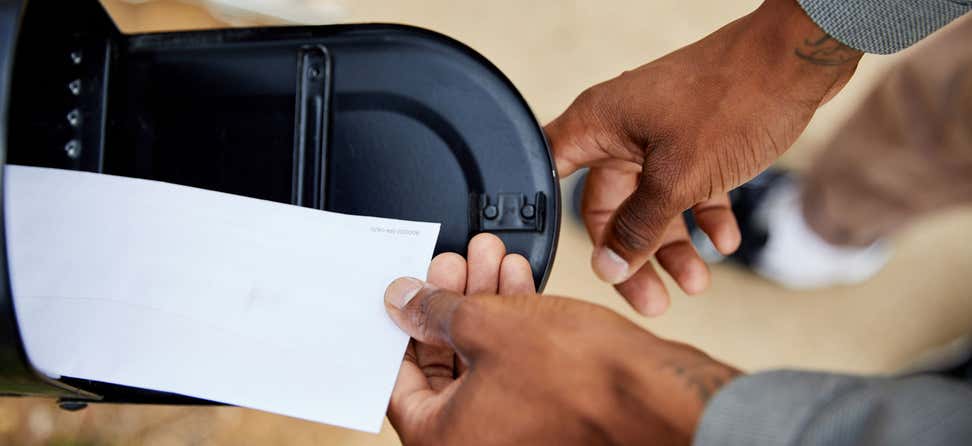 A Black senior man is placing an envelope in a mailbox.
