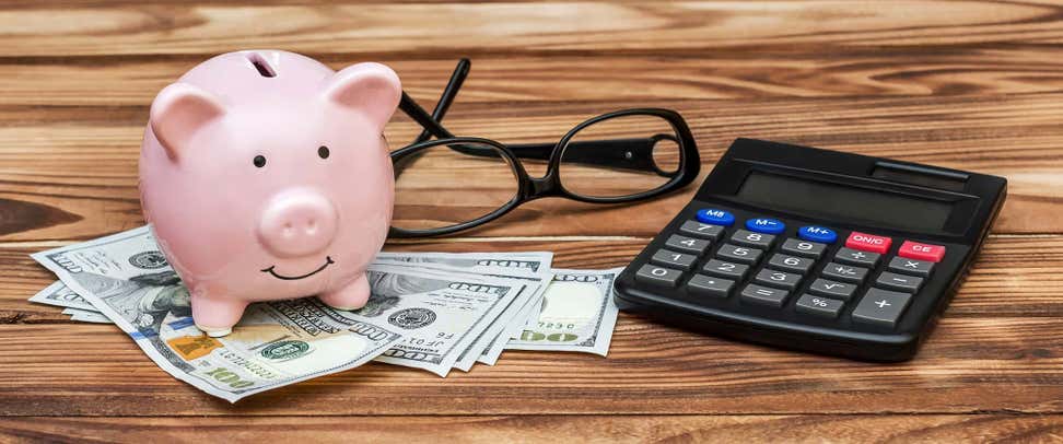 Piggy bank with calculator, money and eyeglasses on the table