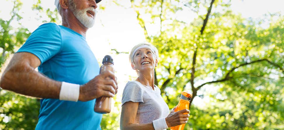 A senior Caucasian couple is out for a run in the park on a sunny day.