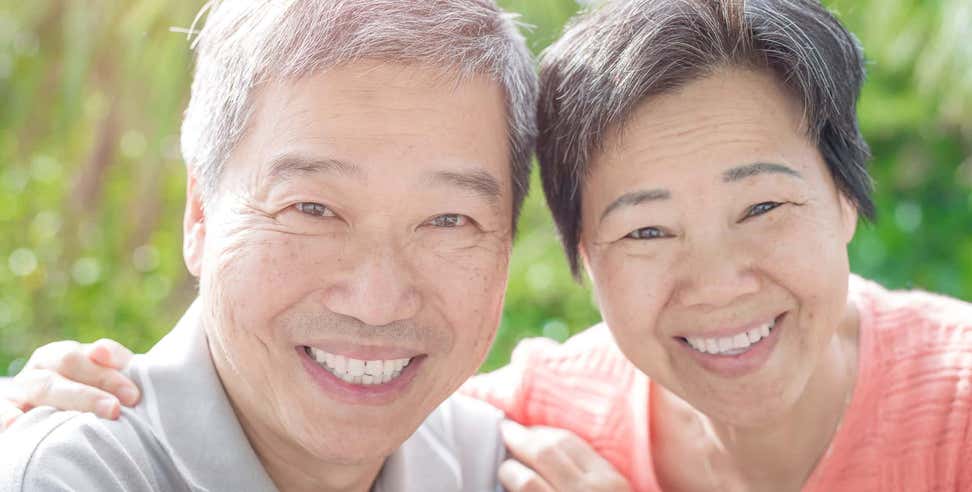 A senior Asian couple is embracing each other, smiling really big for the camera.