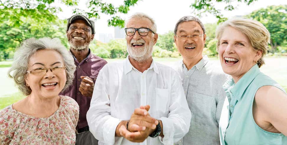 A group of seniors is smiling while outdoors at a park.