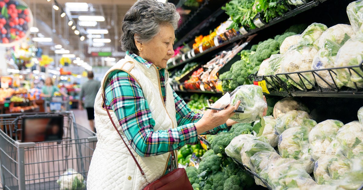 A senior Asian woman is looking at produce in the grocery store.