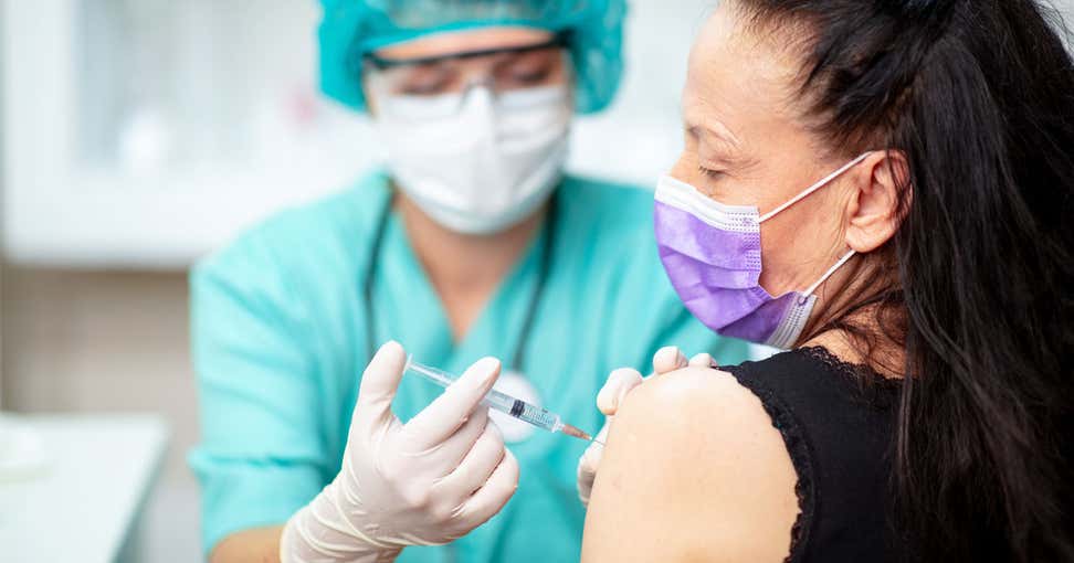 older woman with purple mask receiving vaccine shot in arm