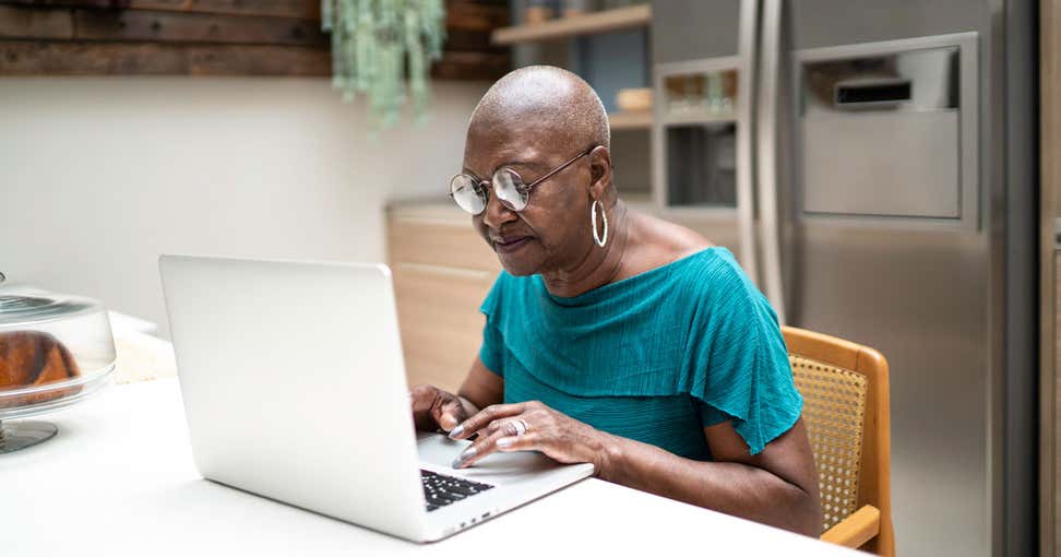 A senior Black female is using her laptop at her kitchen table, thinking about how to create a great password for her email.
