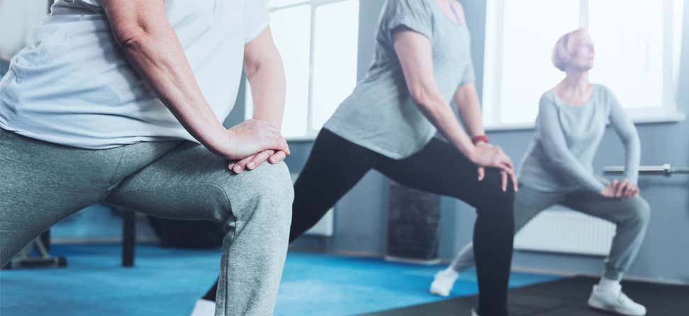 An upclose shot of a group of senior ladies standing in a row and doing lunging exercises while training in a gym.