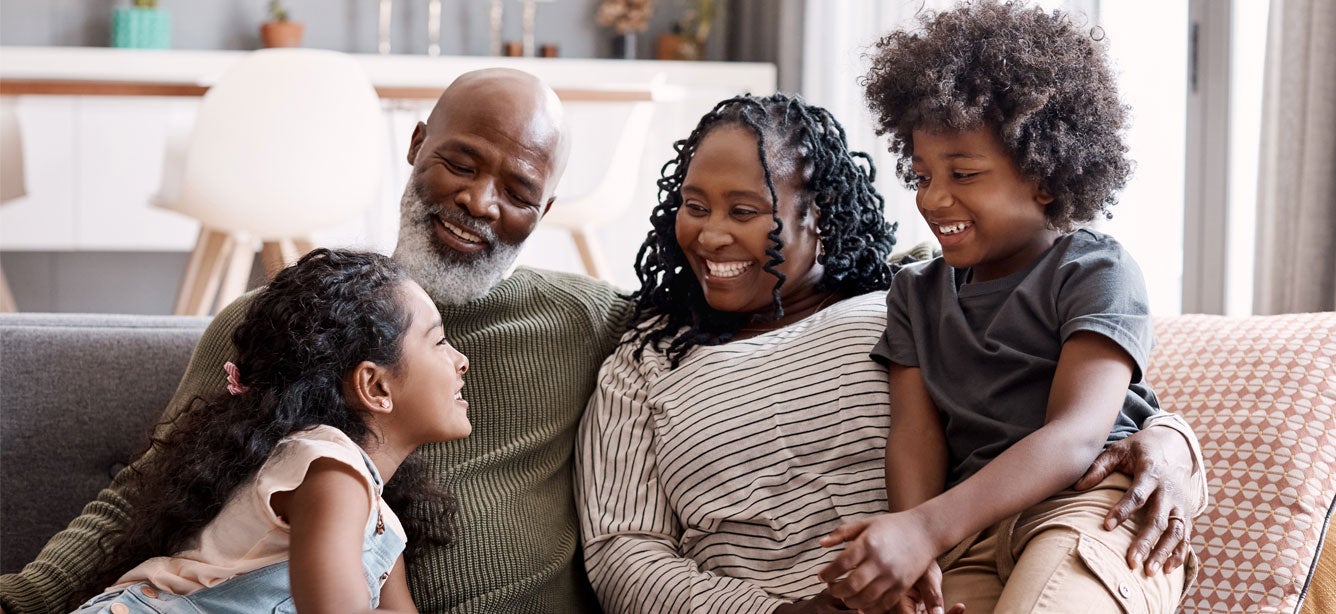 A happy Black, intergenerational family is sitting on the couch at home.