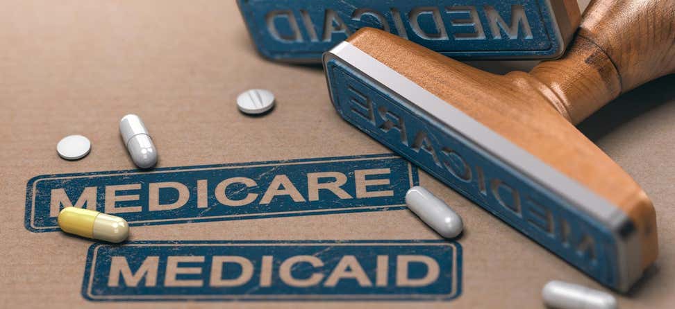 A close up shot of "Medicare" and "Medicaid" stamped on cardboard, along with a smattering of prescription pills.