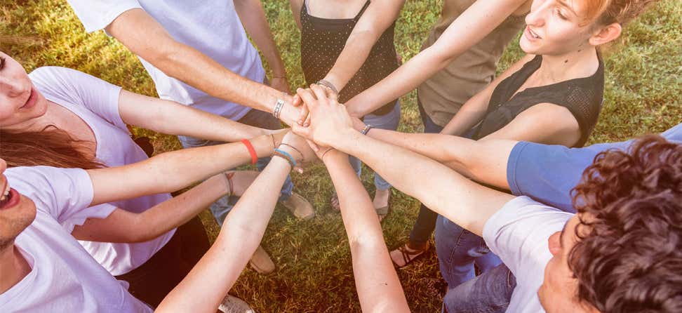 A group of multi-generational people have their hands in a huddle, signifying teamwork.