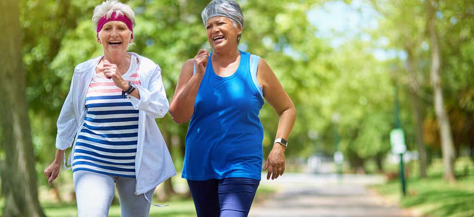 Two senior women are walking briskly in the park, smiling while exercising.