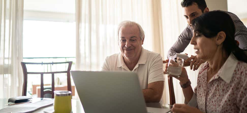 An older Hispanic couple, alongside their son, are looking at a computer, discussing their financial situation together.
