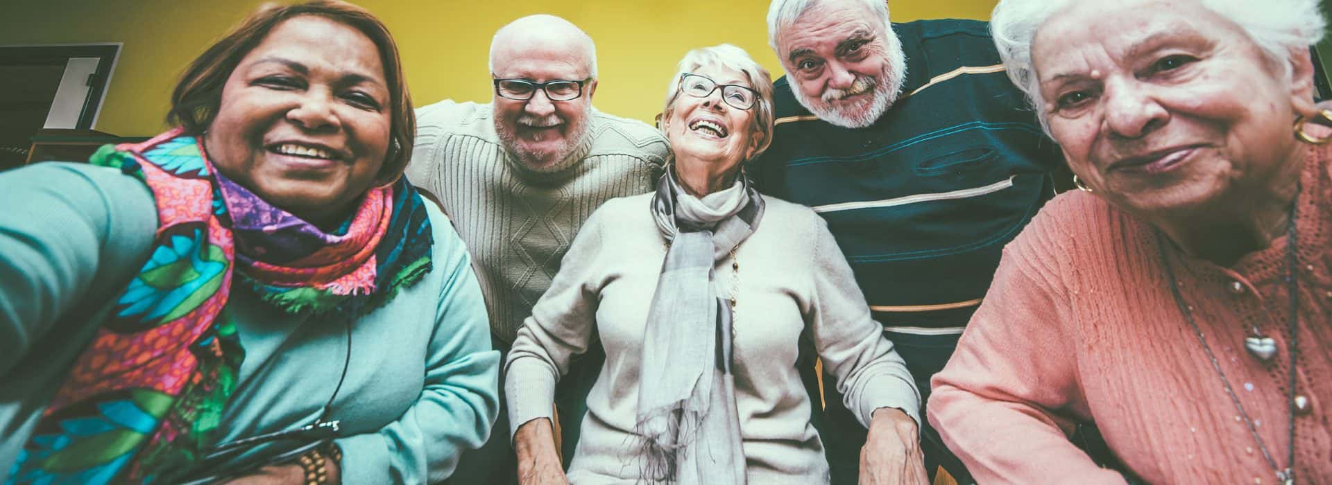 A group of multi-ethnic seniors pose for the camera at a senior center.