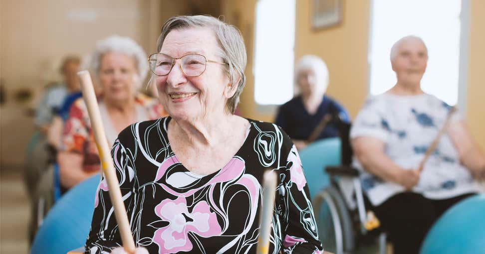 A senior caucasian woman is in a senior center, playing with a drumstick during a group activity.