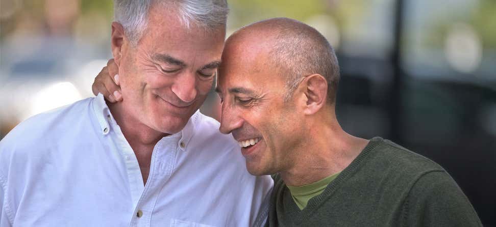 An elderly gay caucasian couple smile while embracing each other.