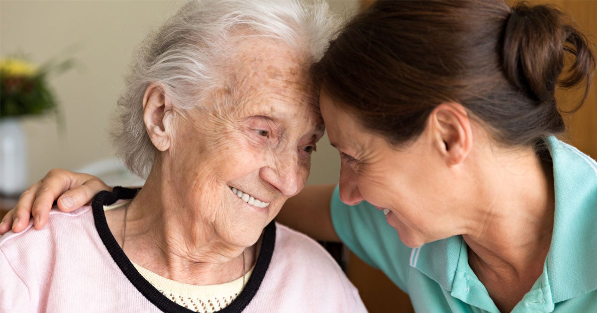 A senior woman smiles, hugging her caregiver during her house visit.
