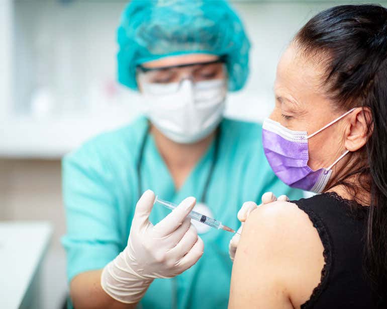 older woman with purple mask receiving vaccine shot in arm