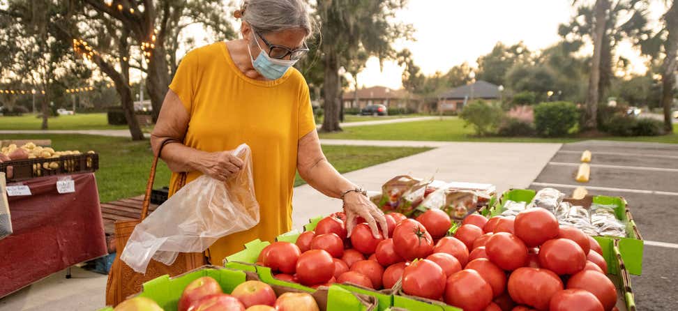 A senior Hispanic woman wearing a mask is shopping at a farmer's market picking out fresh produce.